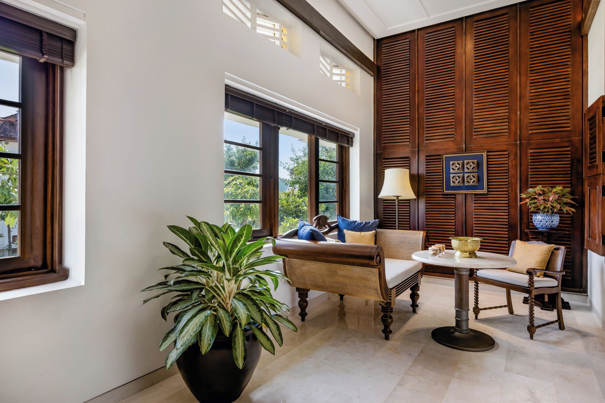 A room with a large potted plant, a sofa, a round table, and a lamp.