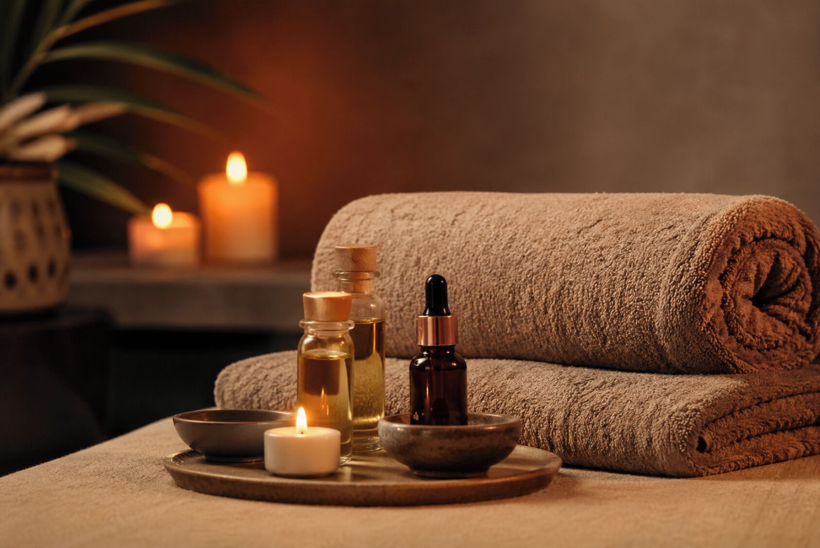 Wellnessbereich mit gerolltem Handtuch, Kerzen und ätherischen Ölen auf einer Ablagefläche.