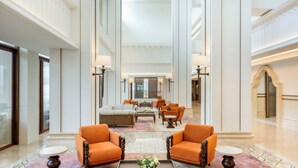 A spacious lobby with high ceilings, a central seating area with orange chairs, a coffee table with a floral centerpiece, and a patterned floor. - Grand Hotel De Djokja (Yogyakarta)