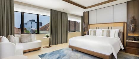 Una habitación de hotel moderna con una cama grande, un sofá, una mesita con una planta y vistas a edificios a través de amplias ventanas.