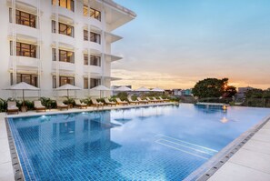 A swimming pool with lounge chairs and umbrellas, surrounded by a modern building with multiple floors and balconies. - Grand Hotel De Djokja (Yogyakarta)