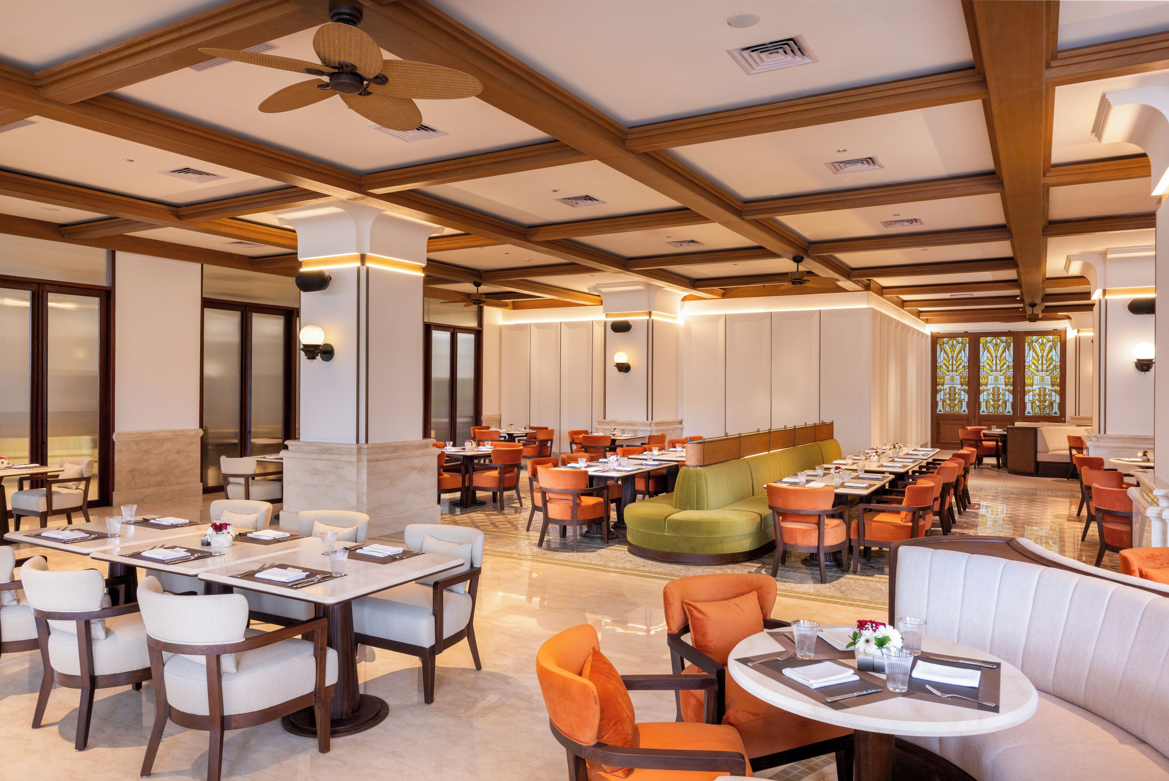 A spacious dining area with multiple tables and chairs, a green sofa, and a ceiling fan.