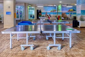 Une table de ping-pong sur roulettes, installée dans un hall d’entrée, avec une fresque murale représentant une scène de plage.