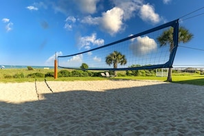 Una red de voleibol de playa sobre arena, con un cielo despejado y palmeras al fondo.