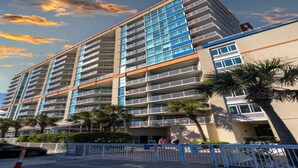 Un hôtel à plusieurs étages doté de balcons, de palmiers et surplombant un ciel dégagé.