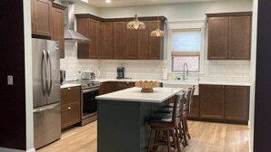 A modern kitchen with dark wooden cabinets, stainless steel appliances, a central island with bar stools, and pendant lighting.