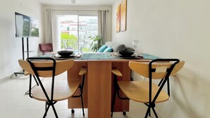 A dining area with a wooden table and four chairs, a ceiling fan, and a view of buildings through a large window. - Local atmosphere great location 2 bedroom, Fast WiFi Ideal for long stays. (Cancún)