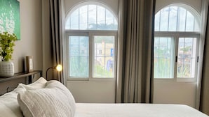 A bedroom with a large bed, two windows with curtains, a bedside table with a lamp, and a wall-mounted plant. - Local atmosphere great location 2 bedroom, Fast WiFi Ideal for long stays. (Cancún)
