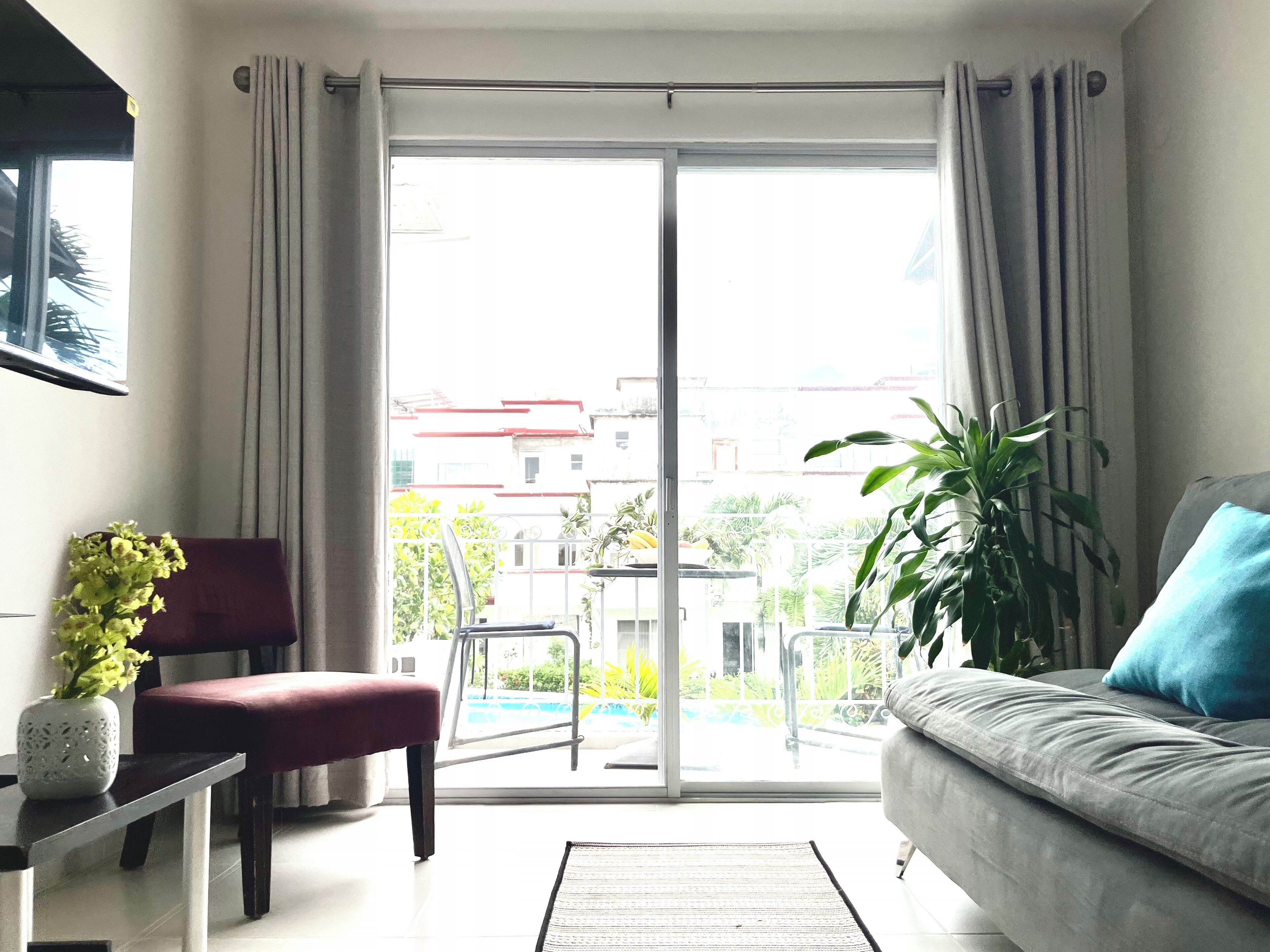 Un salon comprenant un canapé, un fauteuil, une petite table avec une plante, et une porte-fenêtre coulissante donnant sur un espace extérieur avec une piscine et de la verdure.