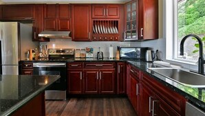 Una cocina moderna con armarios de madera oscura, electrodomésticos de acero inoxidable y un ventanal con vistas a la vegetación.