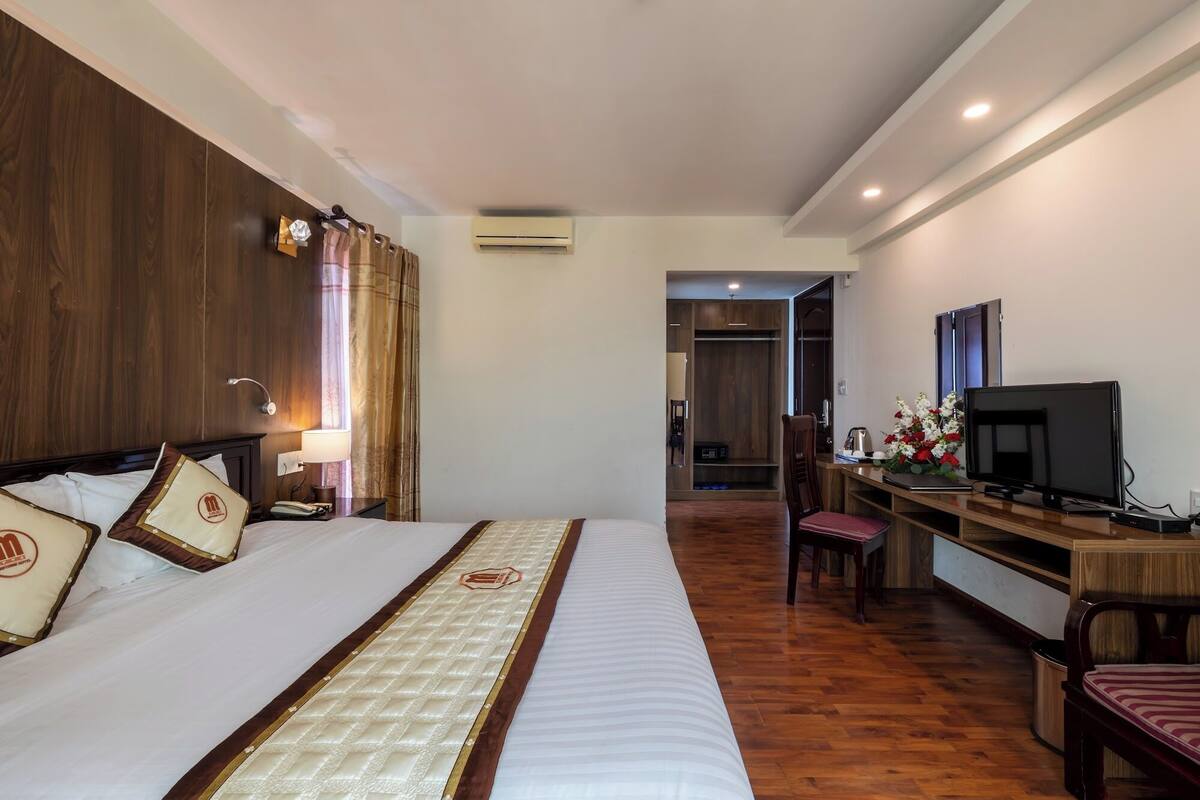 A hotel room with a large bed, a desk with a TV, and a chair.