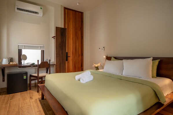 A hotel room with a bed, a desk with a chair, a small refrigerator, and a wooden door. - HÔM Stay - Phố đi bộ (Hue)