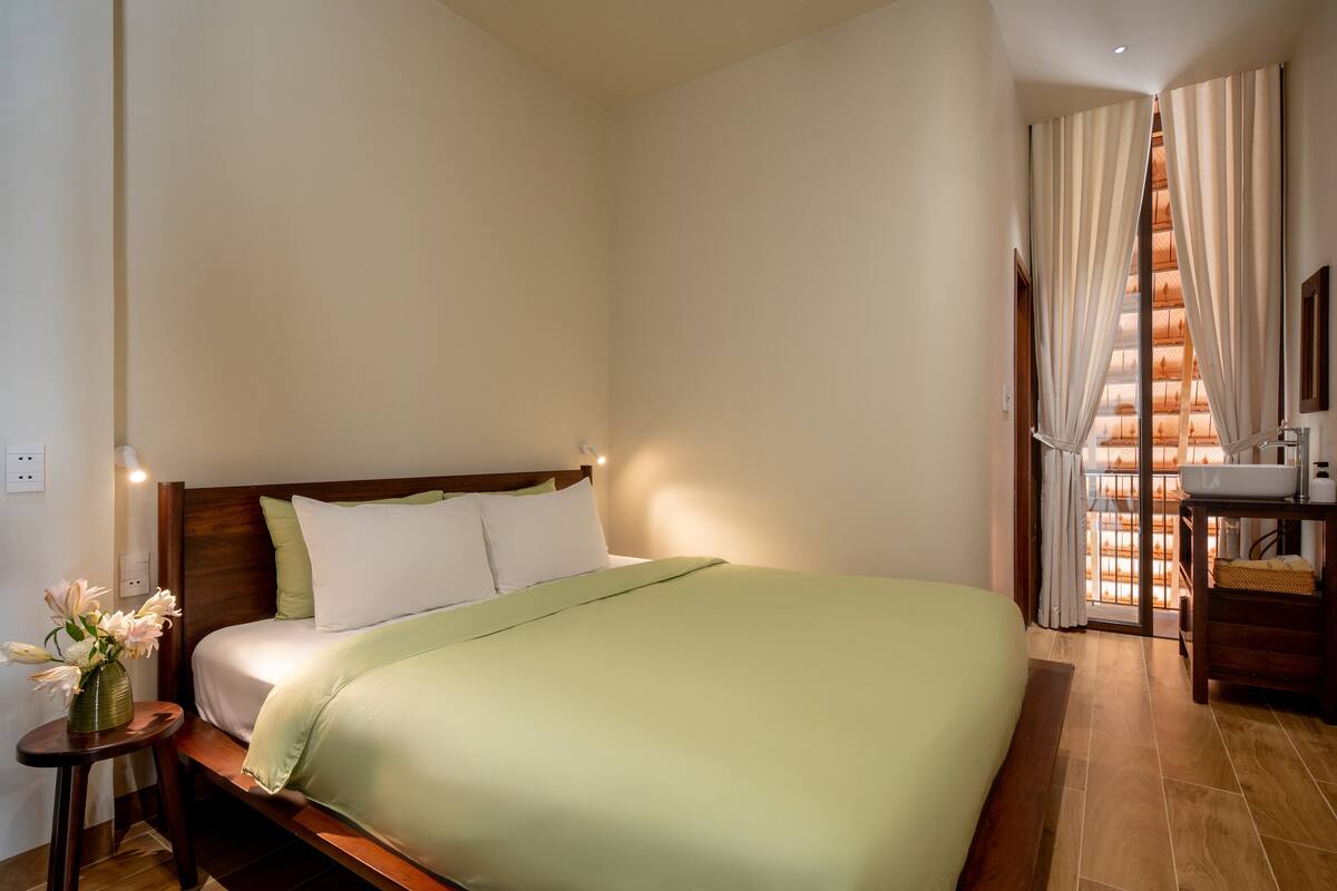 A hotel room with a bed, a nightstand with a vase of flowers, a wooden headboard, and a view of a staircase.