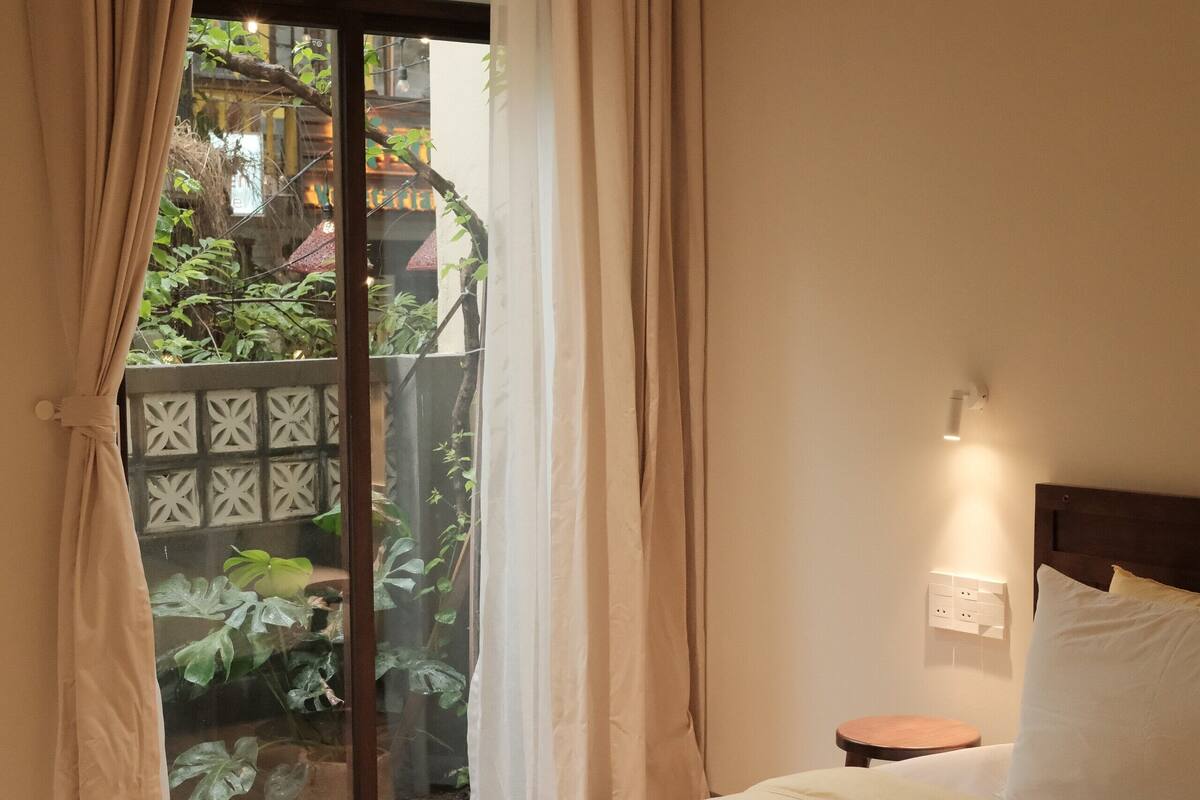A bedroom with a large bed, a sliding glass door to a garden, and a small bedside table with a lamp.