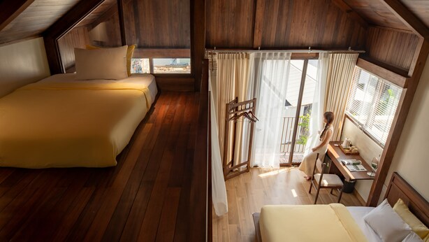 Een slaapkamer met twee bedden, houten vloeren en uitzicht naar buiten door een raam met gordijnen.