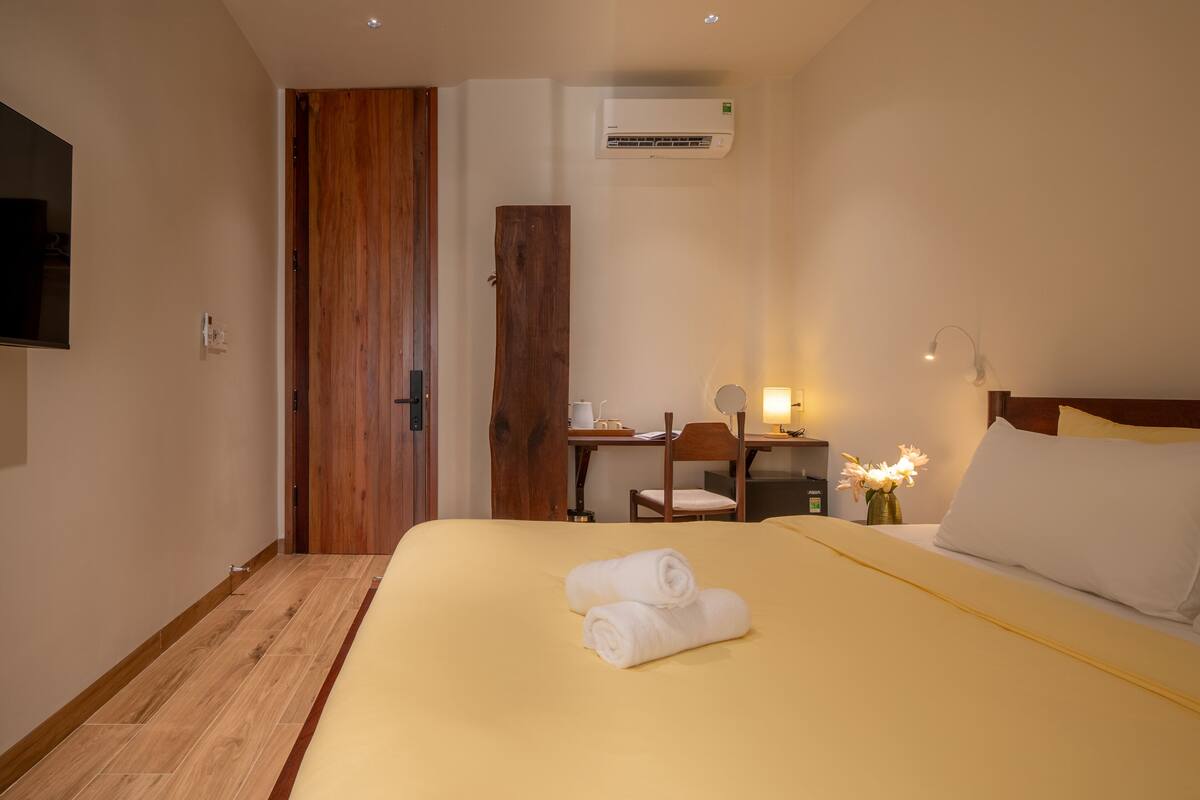 A hotel room with a bed, a desk, a chair, and an air conditioning unit.