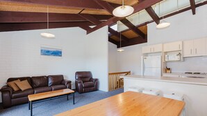 A modern kitchen with white cabinets, a refrigerator, and a microwave. There is a wooden dining table and two leather chairs. - Alpha Centauri - 8/39 Gippsland Street (Jindabyne)