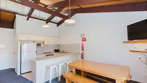 A compact kitchen with white cabinets, a microwave, a stove, and a sink. There is a wooden bench and stools at the counter. - Alpha Centauri - 8/39 Gippsland Street (Jindabyne)