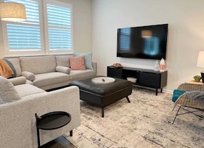 A living room with a sofa, ottoman, TV, and a small side table.