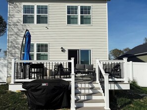 A two-story house with a deck, outdoor furniture, and a covered grill area.