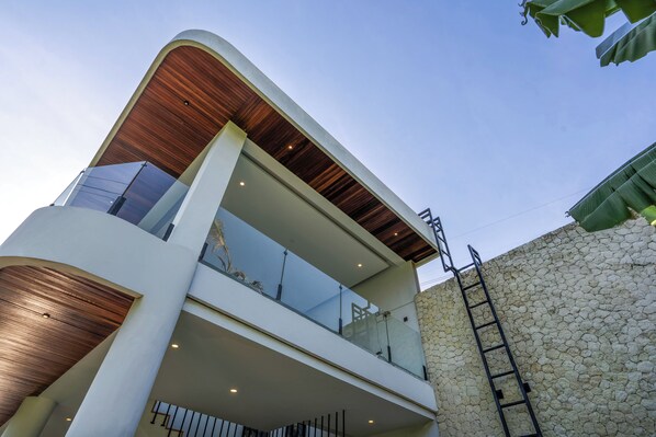 A modern multi-story building with a curved facade, large glass windows, and a stone wall on one side.