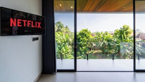 A modern living room with a large flat-screen TV mounted on the wall displaying the Netflix logo. - Jungle Breeze Villa by Betterplace (Cepaka)