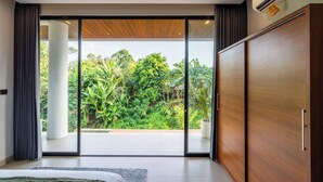 A modern bedroom with a large sliding glass door leading to a balcony with a lush garden view. - Jungle Breeze Villa by Betterplace (Cepaka)