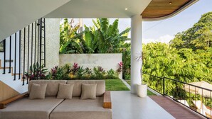 A modern living area with a sofa, a staircase, and a view of lush greenery. - Jungle Breeze Villa by Betterplace (Cepaka)