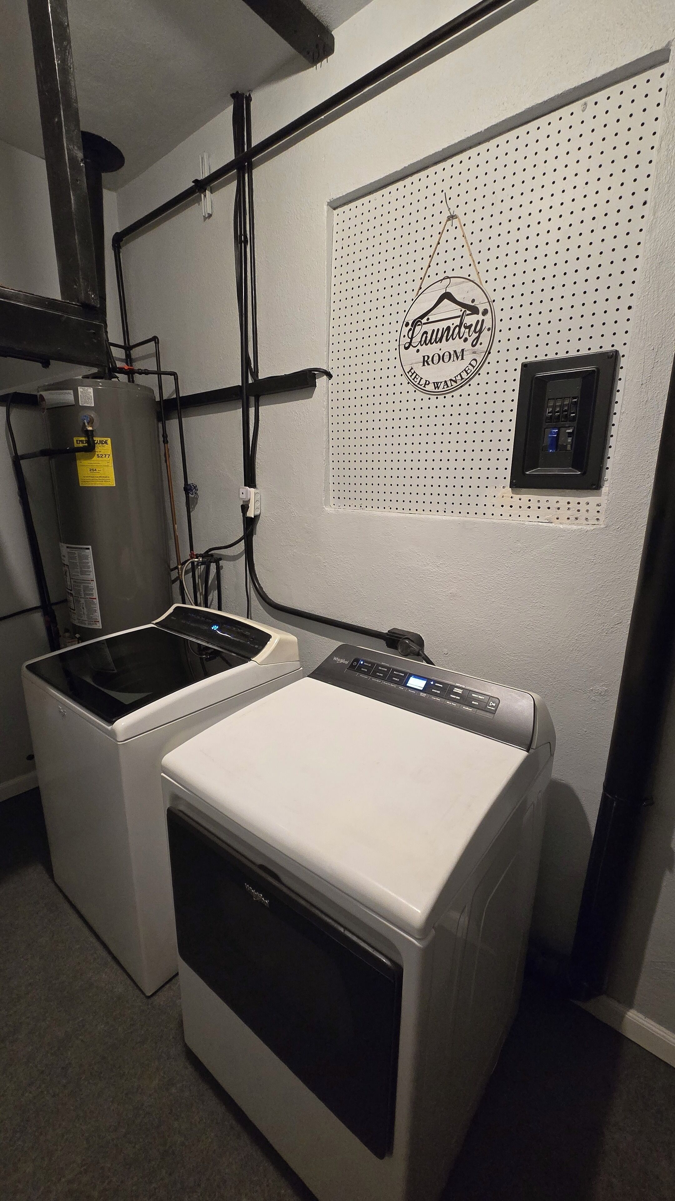 Ein Waschraum mit einer Frontlader-Waschmaschine und einem Trockner, einem Warmwasserbereiter und einem Bedienfeld an der Wand.