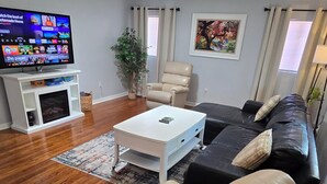 A living room with a white coffee table, beige sofa, and a TV on a stand. - Spacious 3/2 Mt Dora home w/ Hot tub/Private in law suite & Lush fenced backyard (Mount Dora)