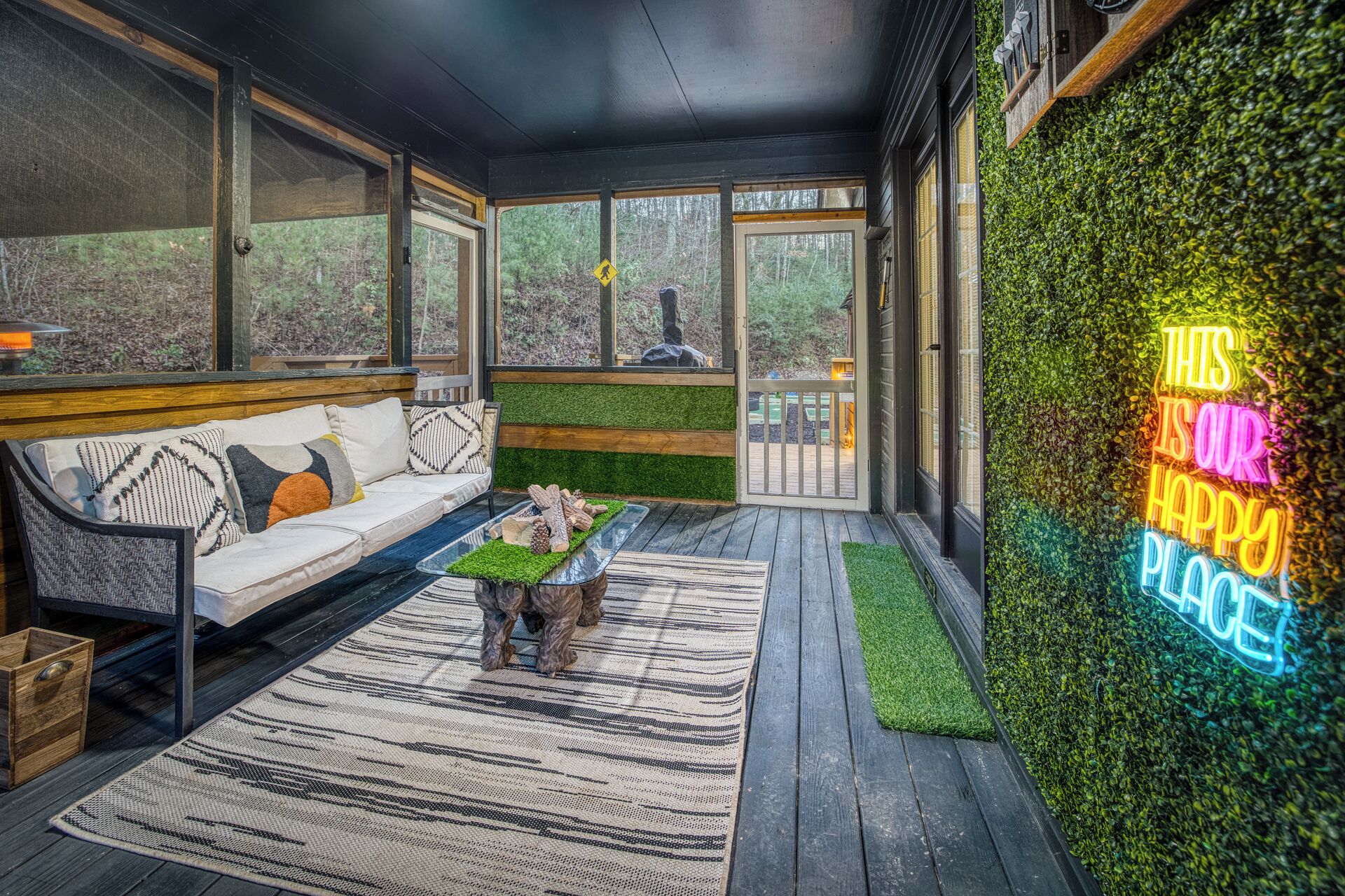Un patio interior acogedor con una terraza de madera, un sofá y un letrero de neón.