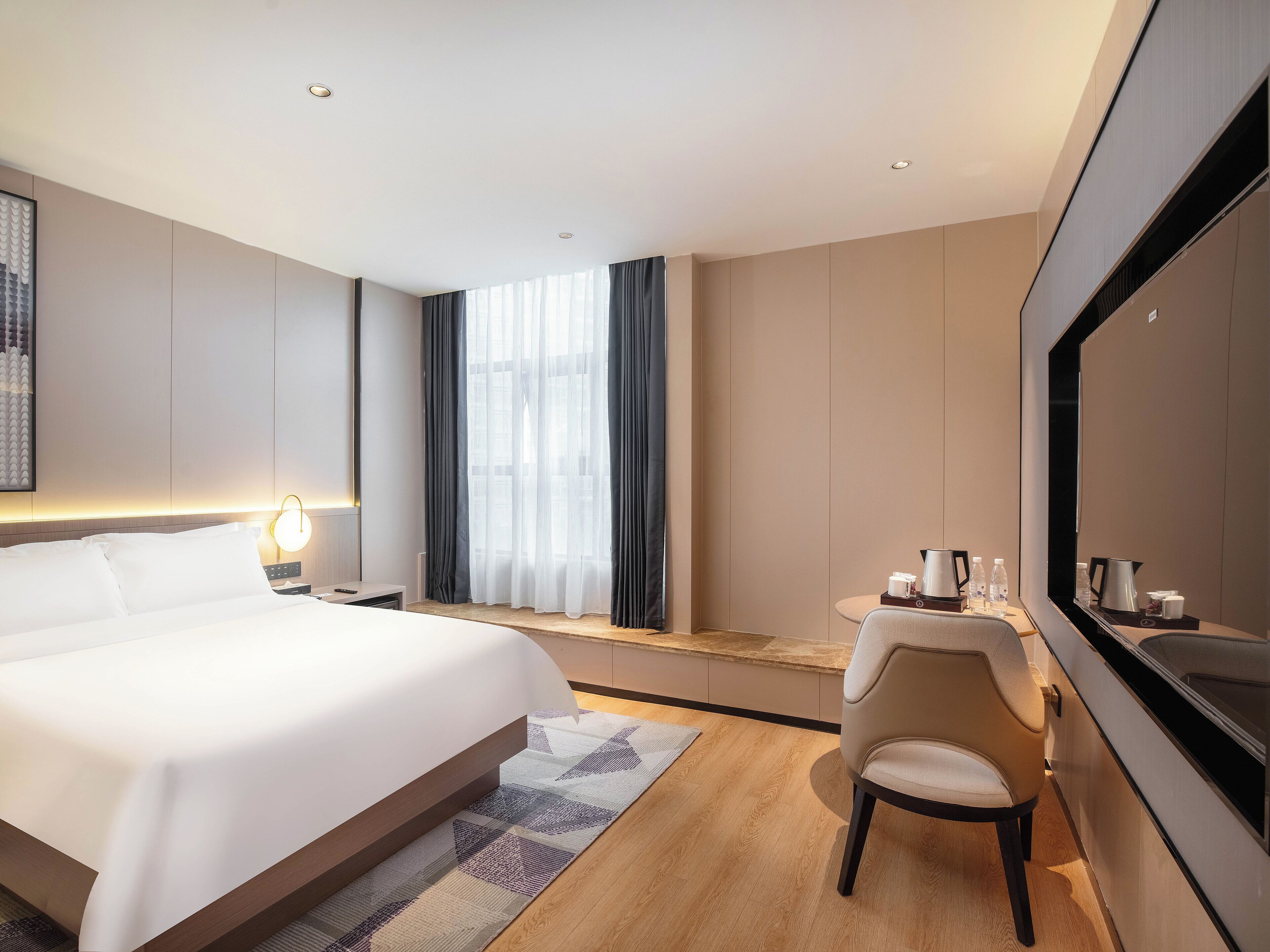 A modern hotel room with a large bed, a desk with a chair, a flat-screen TV, and a large window with curtains.