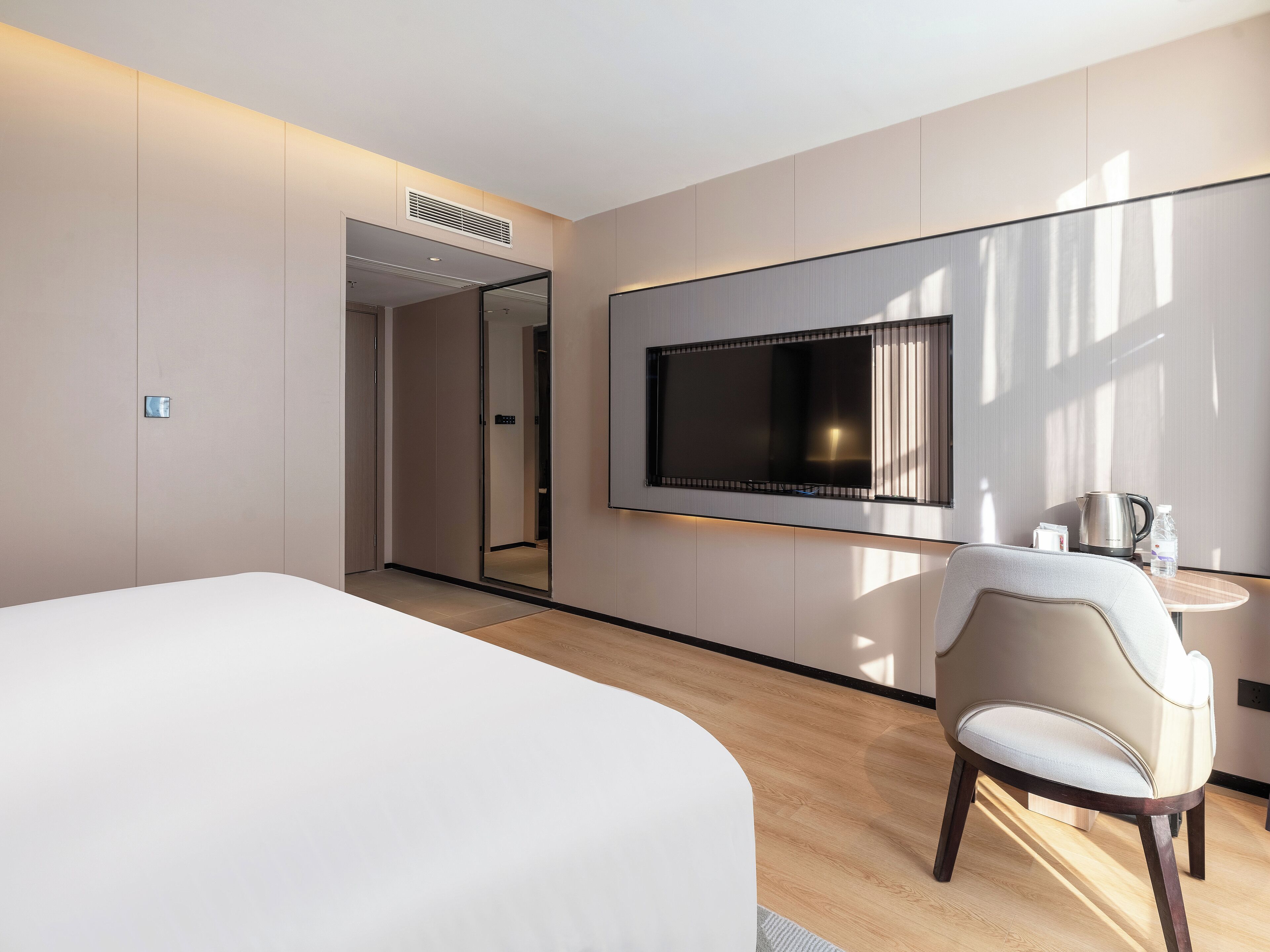 Quarto de hotel moderno com uma cama grande, uma televisão na parede, uma mesa com cadeira e uma cafeteira.
