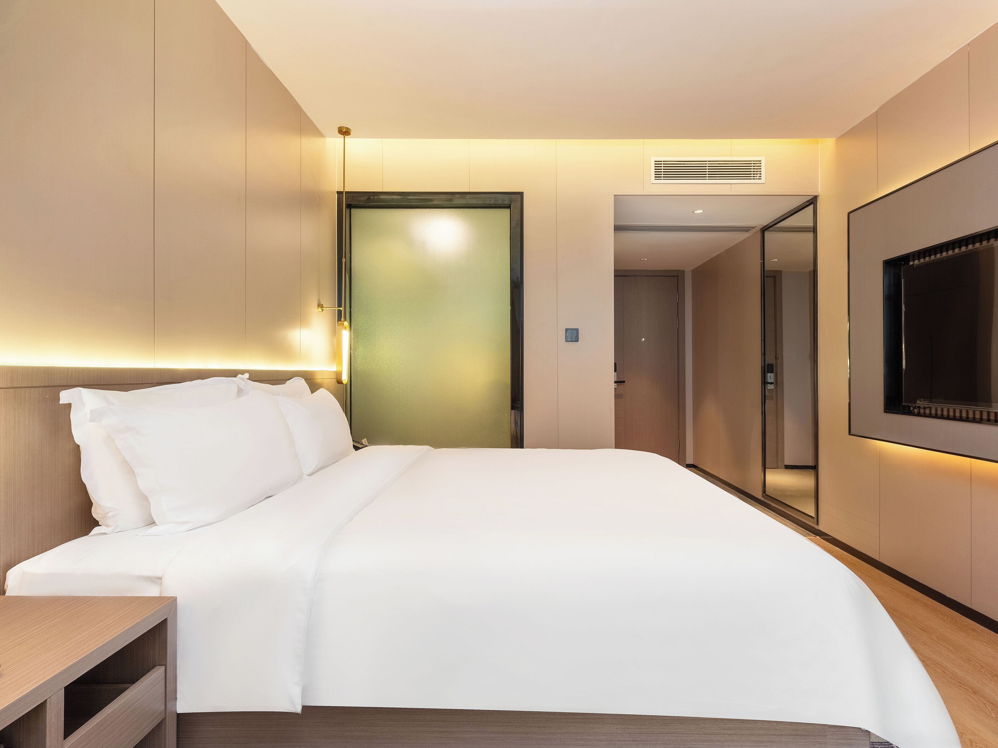 Une chambre d’hôtel avec un grand lit, une table de chevet, un miroir et un téléviseur fixé au mur.