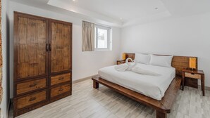 A bedroom with a large wooden wardrobe, a bed with white linens, and a window with curtains. - Sea View 2BR Condo Prime Location C236 (Karon)