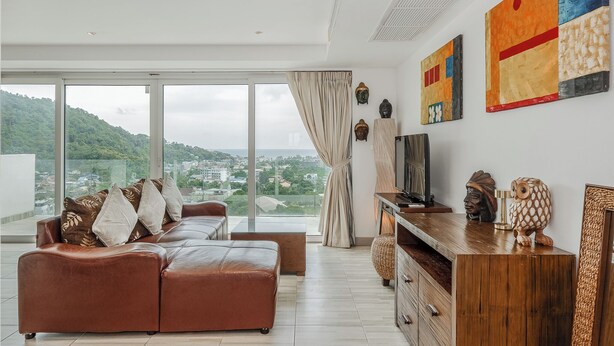 A modern living room with a large sofa, a wooden TV stand, and artwork on the wall. - Sea View 2BR Condo Prime Location C236 (Karon)