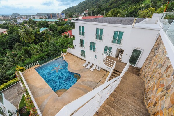 A white building with a swimming pool, surrounded by greenery and a view of a cityscape. - Sea View 2BR Condo Prime Location C236 (Karon)
