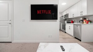 Eine moderne Küche mit weißen Schränken, Edelstahlgeräten und einem an der Wand befestigten Flachbildfernseher, der "NETFLIX" anzeigt.