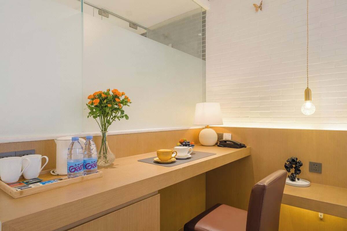 A hotel room with a wooden desk, a vase with flowers, a lamp, and a chair.