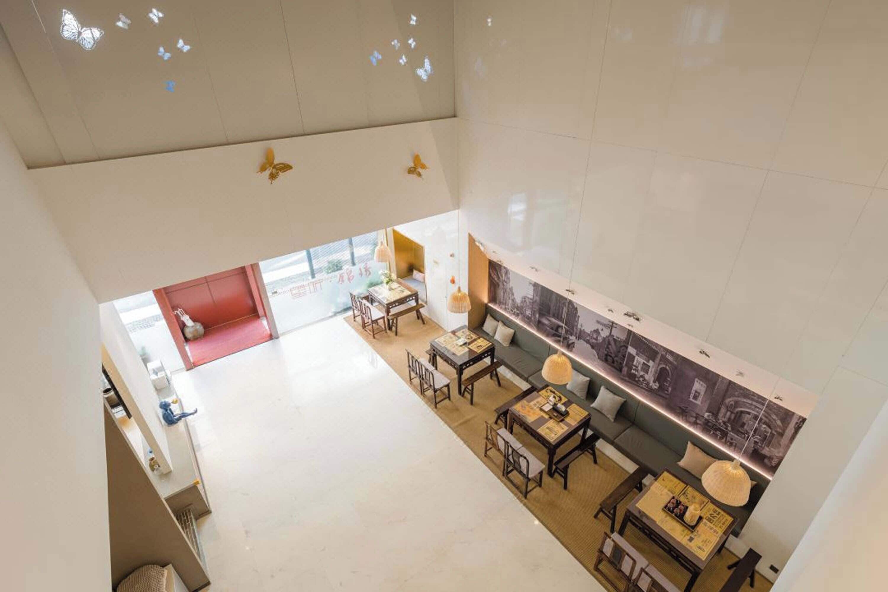 Un hall d’hôtel spacieux avec un plafond haut, un espace détente avec des tables et des chaises, et un grand mur orné d’une fresque représentant un paysage urbain.