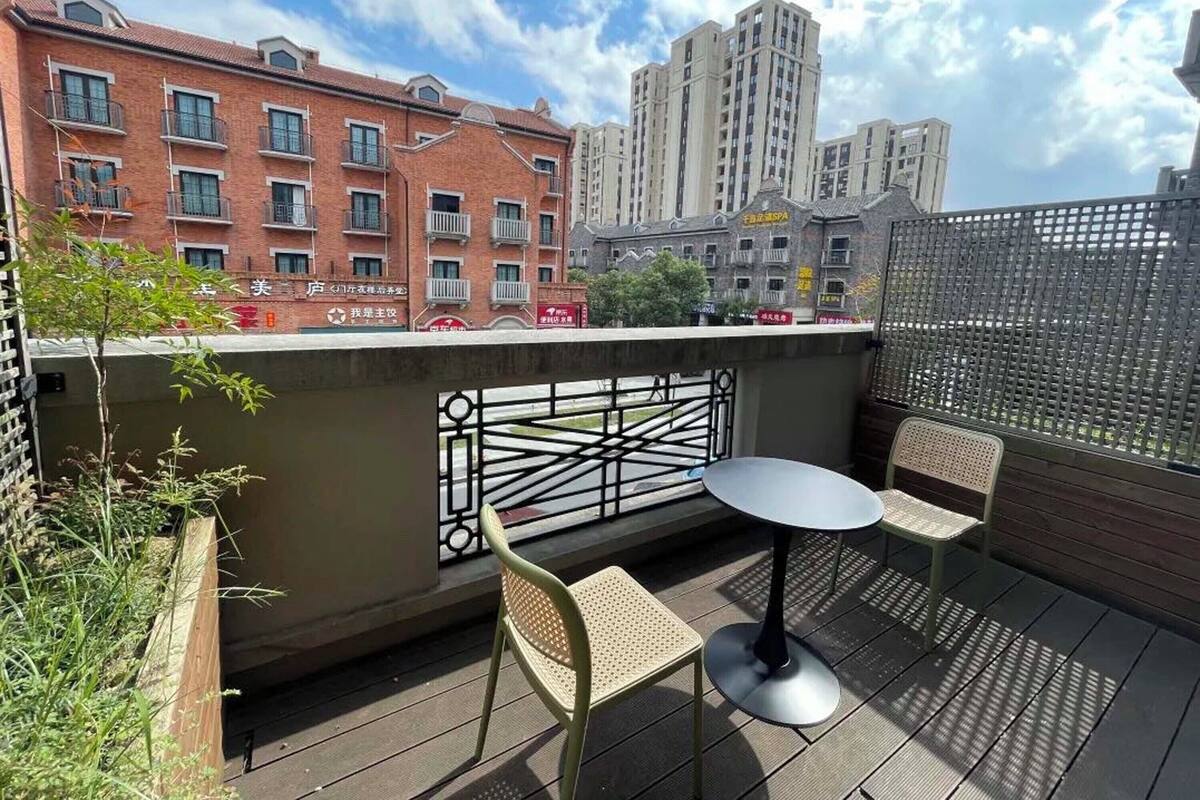 A balcony with a table and two chairs, overlooking a cityscape with buildings and a clear sky.