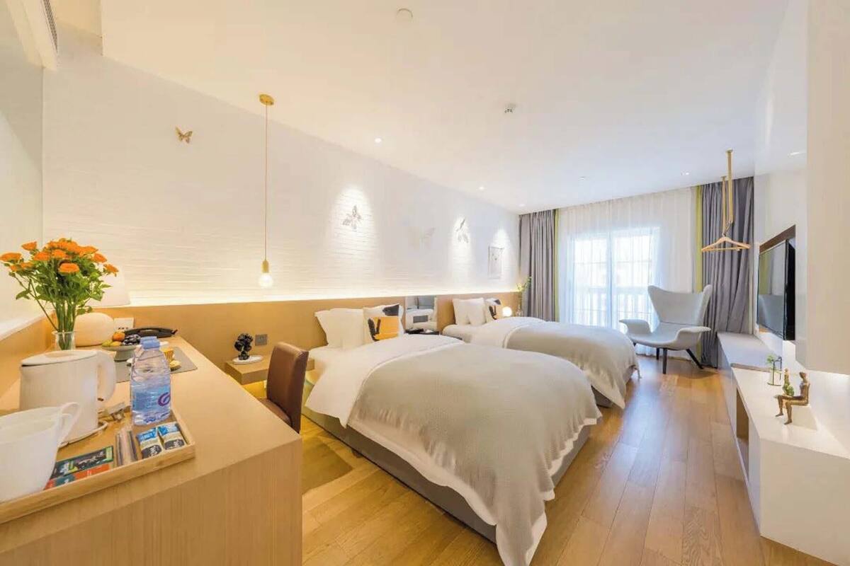 A hotel room with two beds, a desk, a chair, a TV, and a window with curtains.
