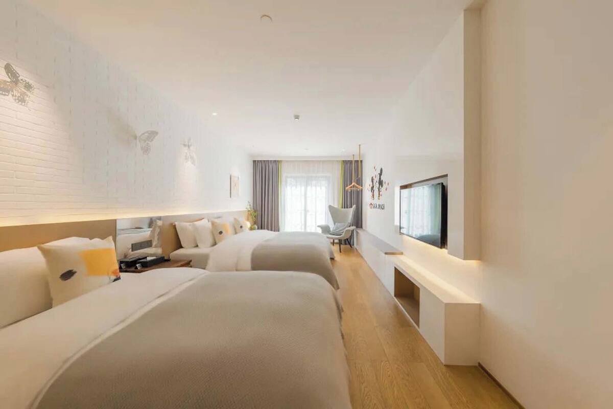 A modern hotel room with two beds, a TV, a desk, and a seating area.