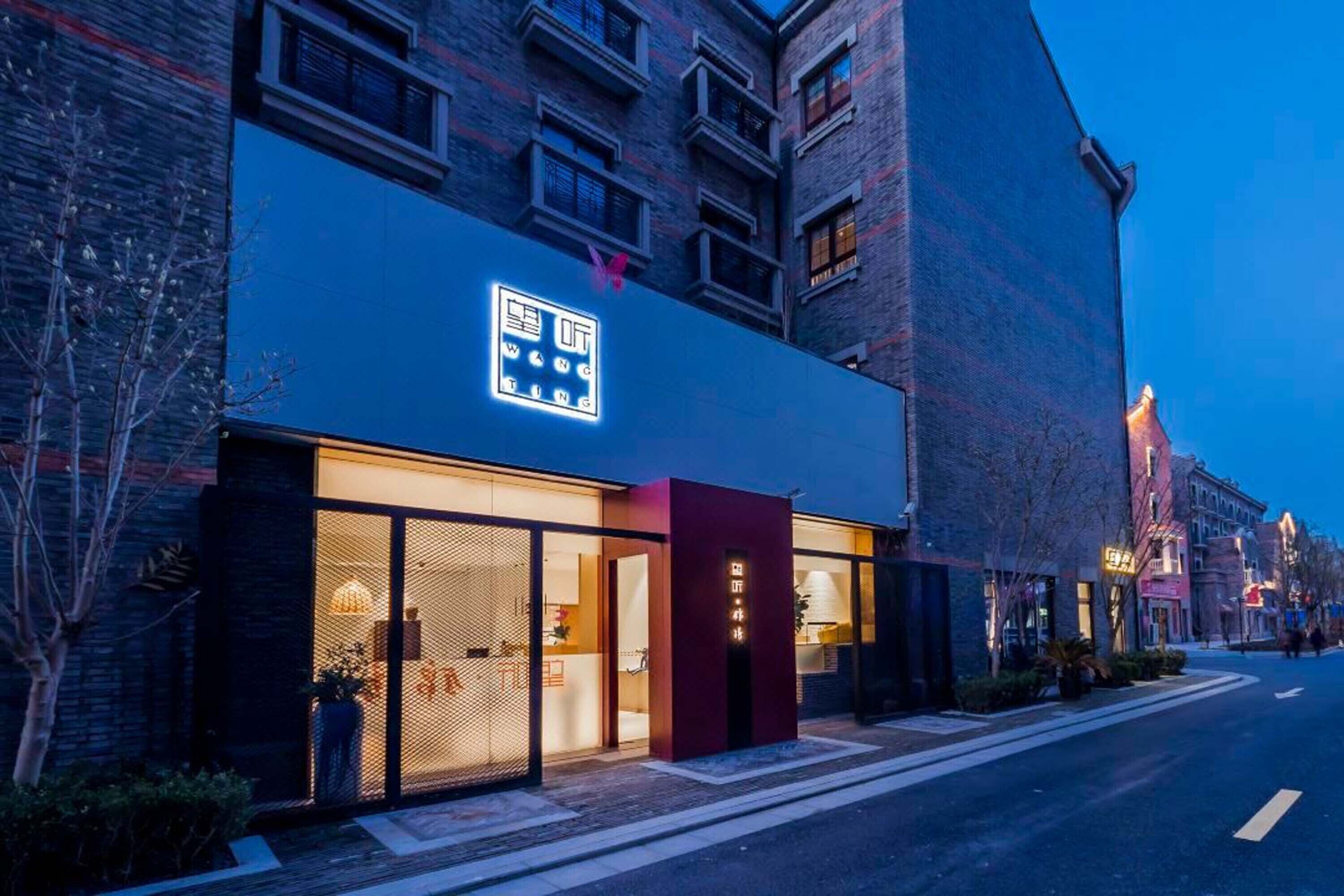 A modern building with a neon sign, large windows, and a red entrance door.
