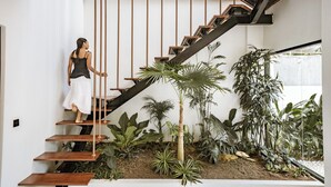 Une femme montant un escalier en bois au design minimaliste, entourée d’une végétation luxuriante.
