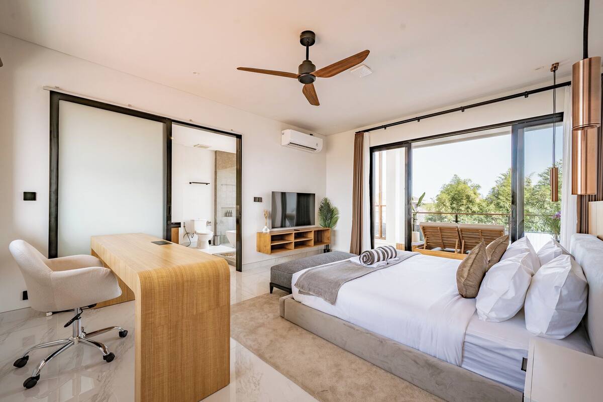 Un dormitorio moderno con una cama grande, un escritorio, una silla, un ventilador de techo y un televisor.