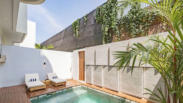 Un espace piscine moderne comprenant deux chaises longues, une terrasse en bois et un mur en pierre agrémenté de verdure.