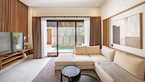 Un salon moderne avec un canapé d’angle, un téléviseur à écran plat et une porte-fenêtre coulissante donnant sur une piscine.