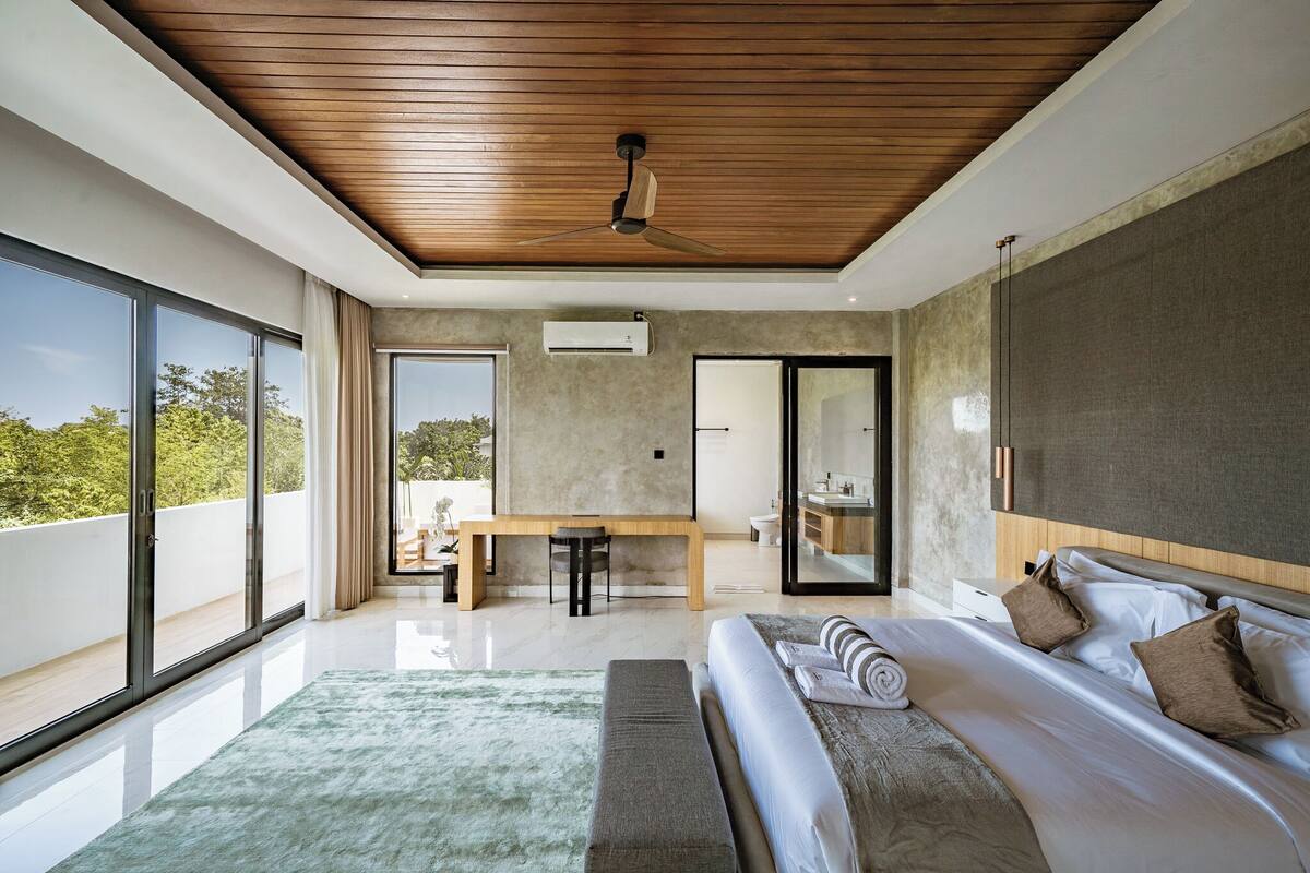 Un dormitorio moderno con una cama grande, un ventilador de techo de madera, un escritorio y vistas al exterior.