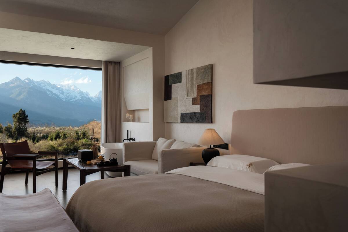A hotel room with a bed, a sofa, a desk, and a chair. There is a window with a mountain view.